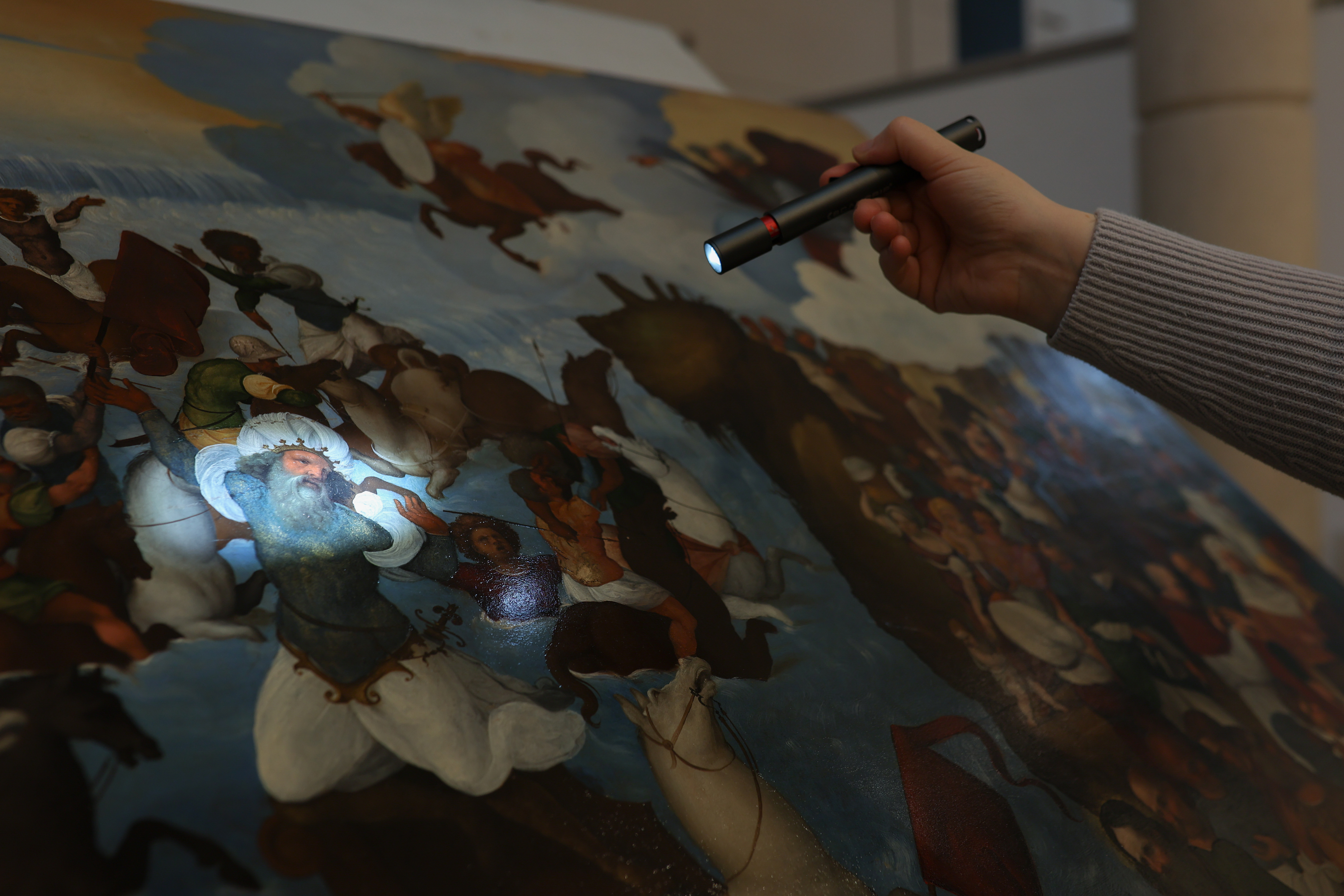 A painting being examined under torchlight