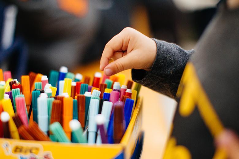 Photo of a child's hand reaching for a coloured marker in a box.