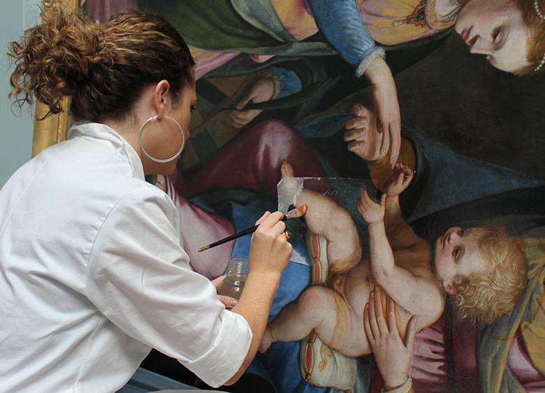 A conservator working on an oil painting