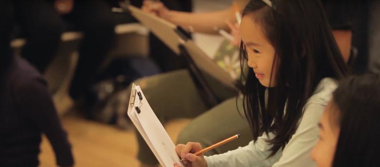 Photo of a girl drawing on a piece of paper on a clipboard.