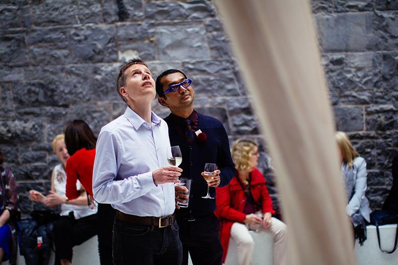 Photography of two men holding glasses of wine while looking a sculpture in a gallery.