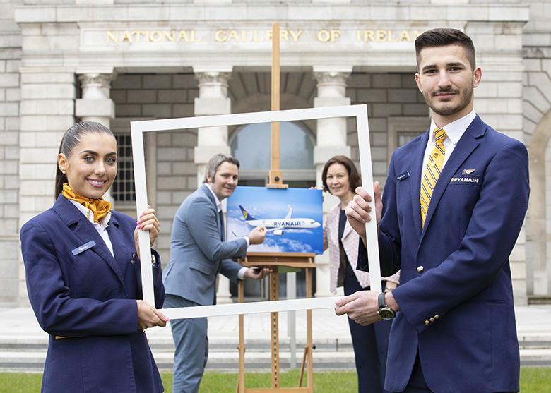 Two Ryanair flight attendants holding a blank picture frame with two people holding a picture of a Ryanair airplane in the background.