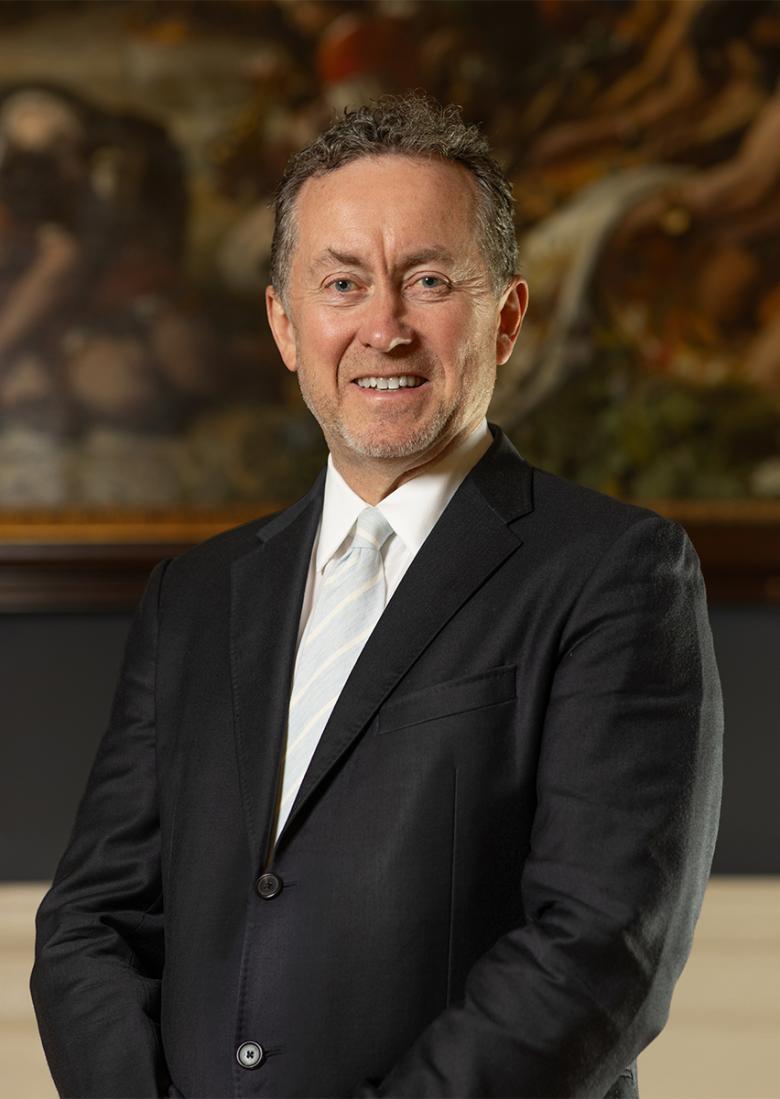 A man in a suit with a white tie in front of a painting