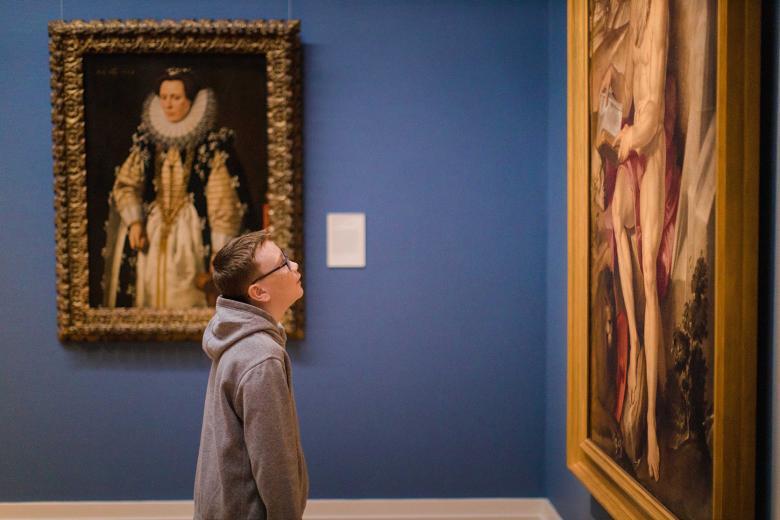 Boy wearing glasses looking at a large gilt-framed painting in a Gallery