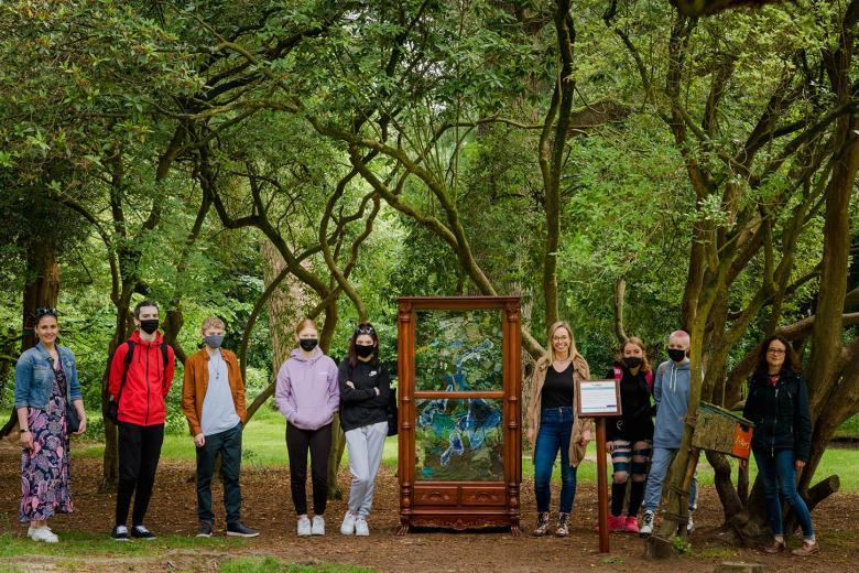 Group of masked young people pose among trees beside a sculpture