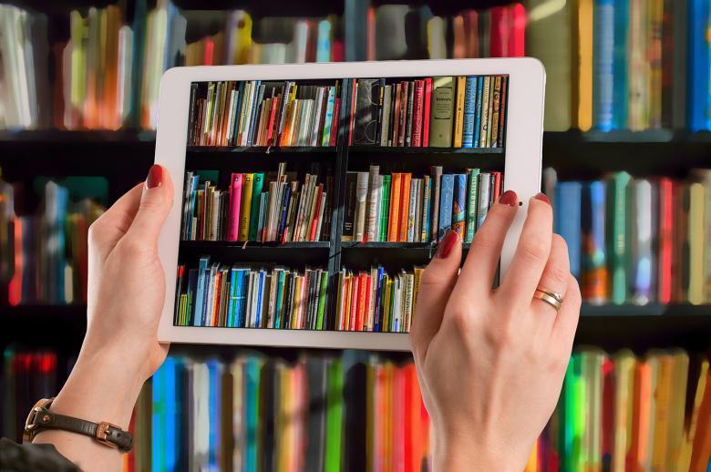 A shelf of colour books, in front of which is held a tablet, which is filming the books