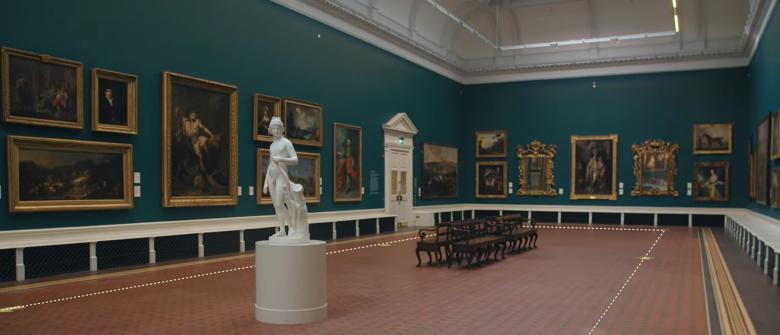 View of the Grand Gallery in the National Gallery of Ireland with gilt-framed paintings on the walls and a white marble statue of a man in the foreground