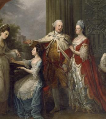 Formal group portrait of five full-length figures: a girl seated at a piano, a girl resting her elbow on top of the piano, an older man gesturing towards the two girls, an older woman standing beside him, and a young Indian page boy leaning in and looking towards them.