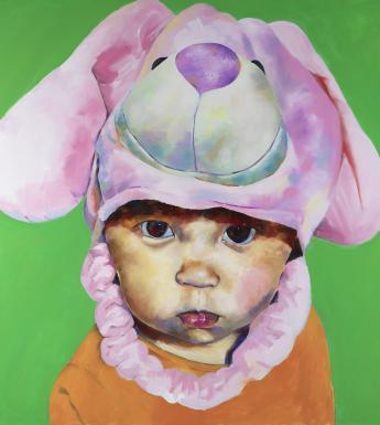 A toddler stares solemnly at the viewer, wearing a hat of a soft toy's head. He stands in front of a vibrant green background, and wears an orange vest.