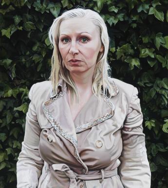 A photorealist painting of a woman standing in a mac. Her hair looks wet, and her coat is damp.