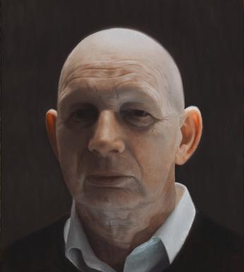 A man stands in shadow. We see his head - he wears a white collared shirt and a dark v-neck jumper.