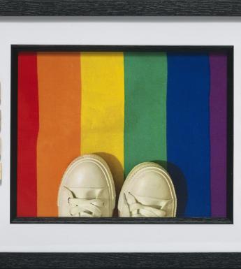 Birds-eye view of white sneakers standing on a rainbow-coloured rectangle. The words like minded are spelled out in Scrabble tiles.