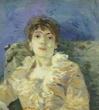 A woman reclines on a patterned divan. She wears a cream dress with orange markings and a ruffled neckline, and drop earrings. The wall behind her is blue.