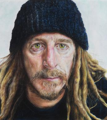 Bust-length portrait of a man with a short beard, blond dreadlocks and wearing a dark woolen hat