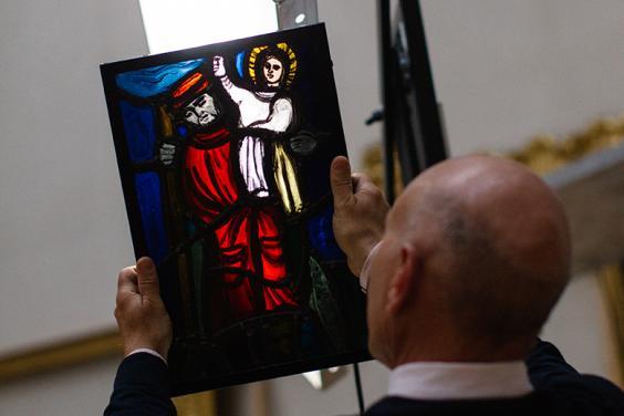 Photo of a man with his back to the camera, holding up a piece of stained glass so that the light shines through it.