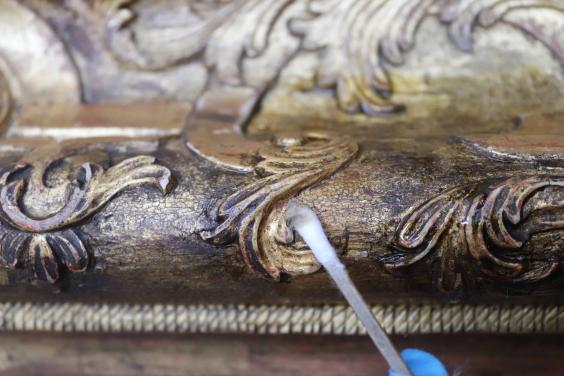 Dirt being removed from a gilded picture frame with a cotton swab