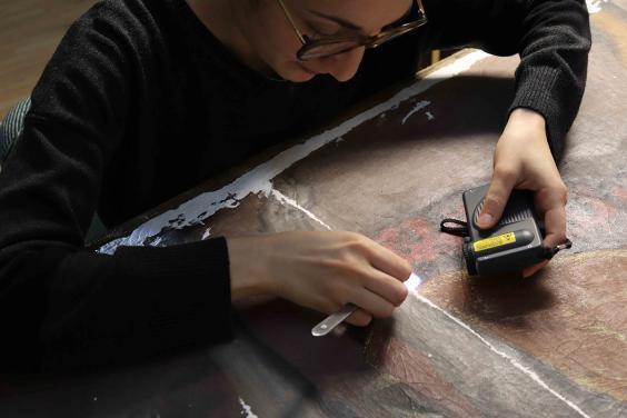 A conservator working on an oil painting